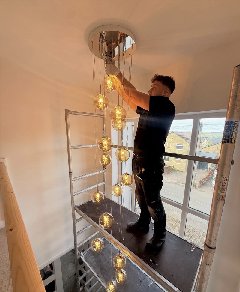Owen Brooke on a scaffold tower, fitting a cascade of glass pendant lights over a stairwell